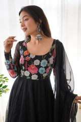 Woman wearing a black dress with colorful floral embroidery indoors.