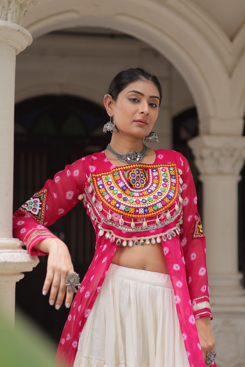 Woman in traditional pink and white outfit with intricate designs, standing in an archway.
