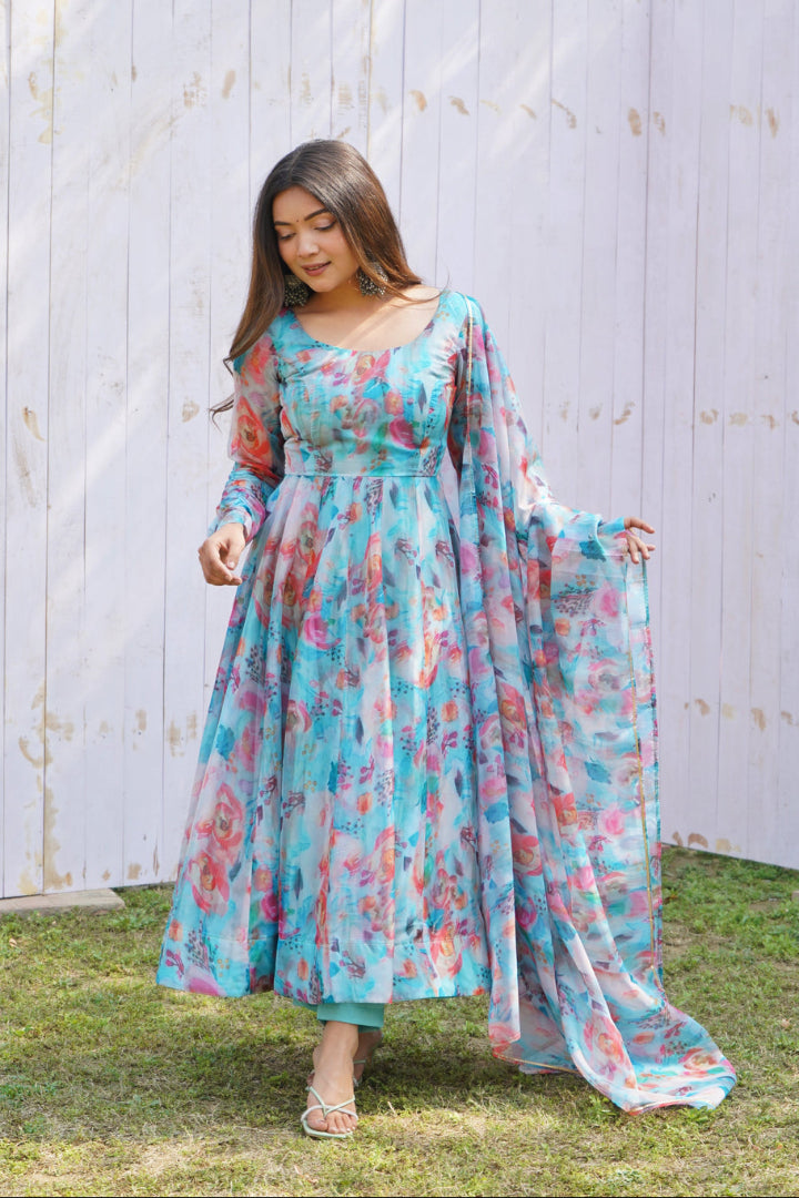 Woman wearing a floral dress with a sheer dupatta against a wooden fence background