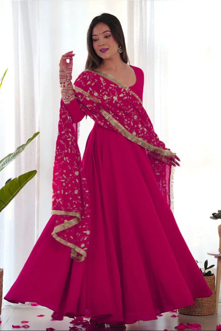 Woman wearing a pink traditional outfit with gold details in a bright room.