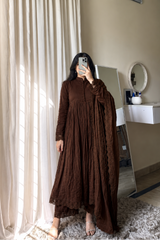 Person wearing a brown dress standing in a room with curtains and a mirror.