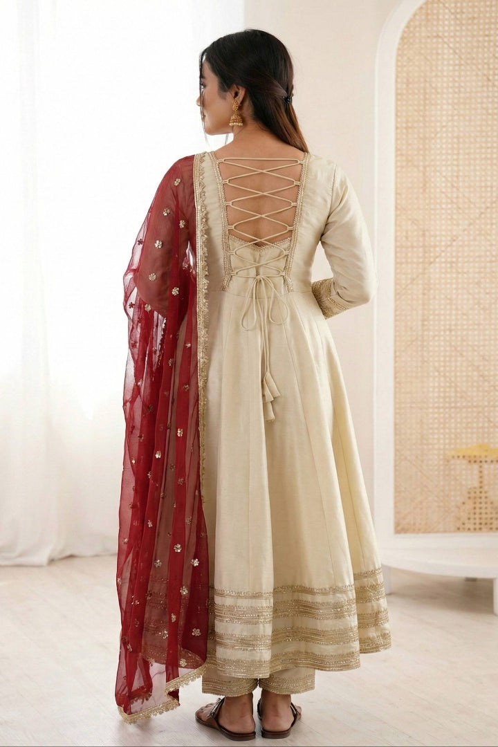 Woman wearing a cream anarkali suit with a red dupatta in a minimalistic room.