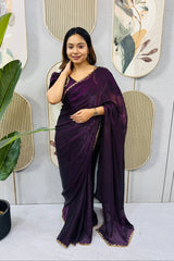 Woman in a purple saree standing next to a plant with decorative wall art in the background
