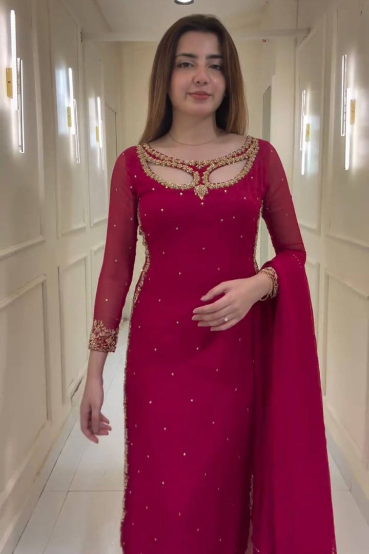 Woman wearing a red traditional outfit with gold embroidery in a hallway.