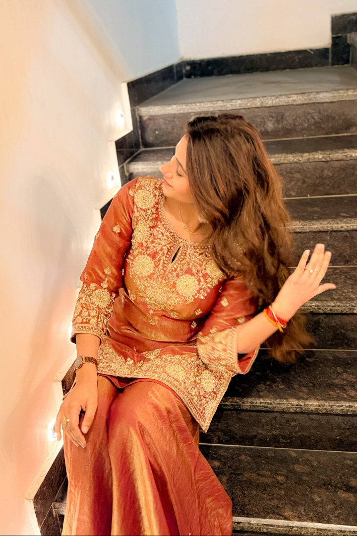 Woman in traditional orange and gold outfit sitting on a staircase