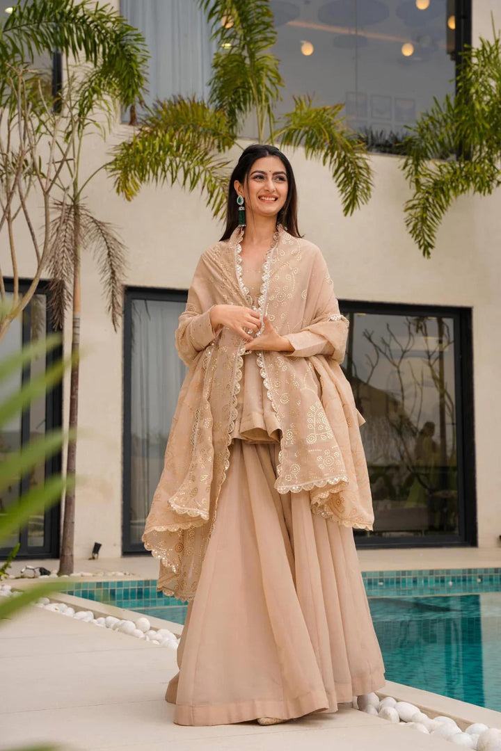 Woman in a beige traditional outfit standing by a pool with greenery around.