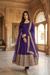 Woman in a purple traditional outfit with gold embroidery standing in an ornate room.