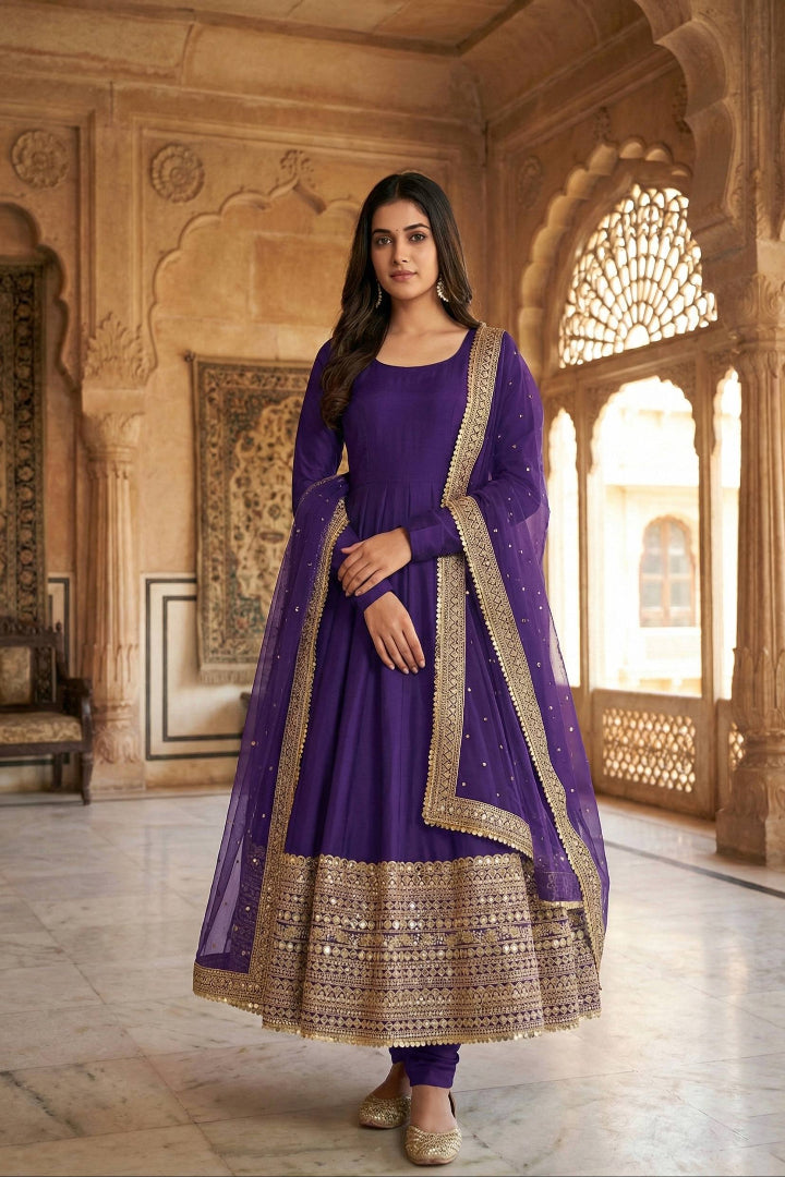 Woman in a purple traditional outfit with gold embroidery standing in an ornate room.