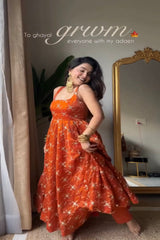 Woman in an orange dress standing in a room with a mirror and plant.