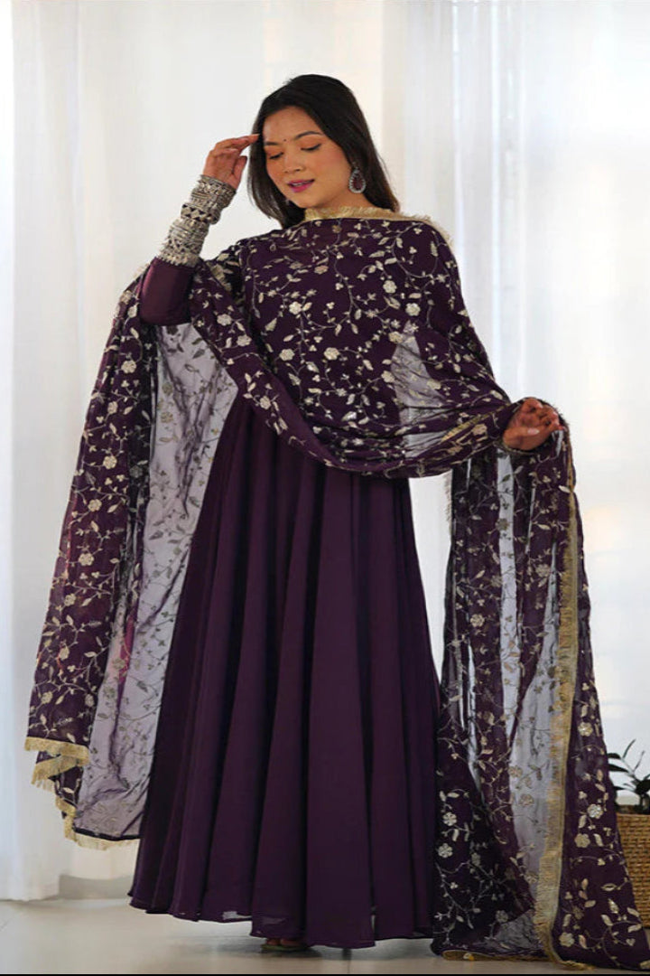 Woman wearing a dark purple traditional outfit with a floral dupatta in a bright room.