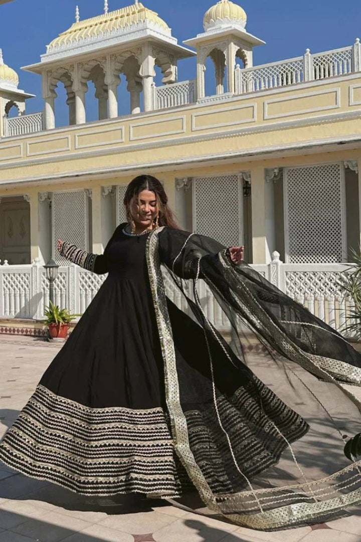 Woman in a black and gold traditional outfit standing in front of a white building with domes.