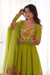 Woman wearing a green floral dress with a sheer dupatta against a white curtain background