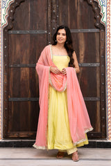 Woman in a yellow dress with a pink dupatta standing in front of a wooden door.