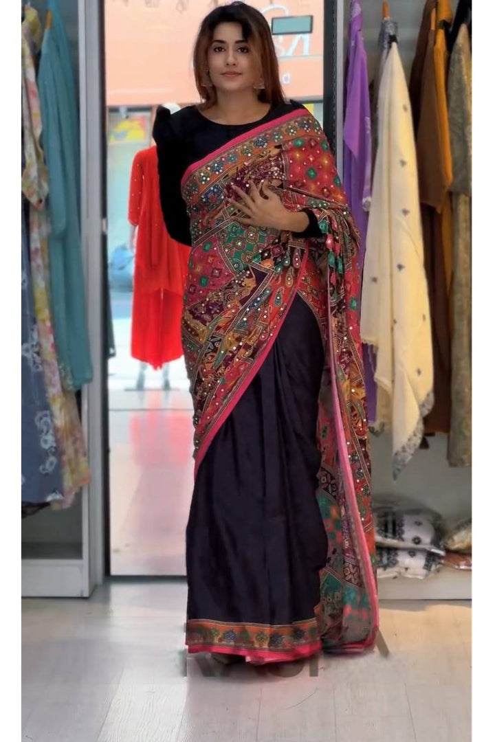 Woman wearing a black saree with a colorful border in a clothing store.