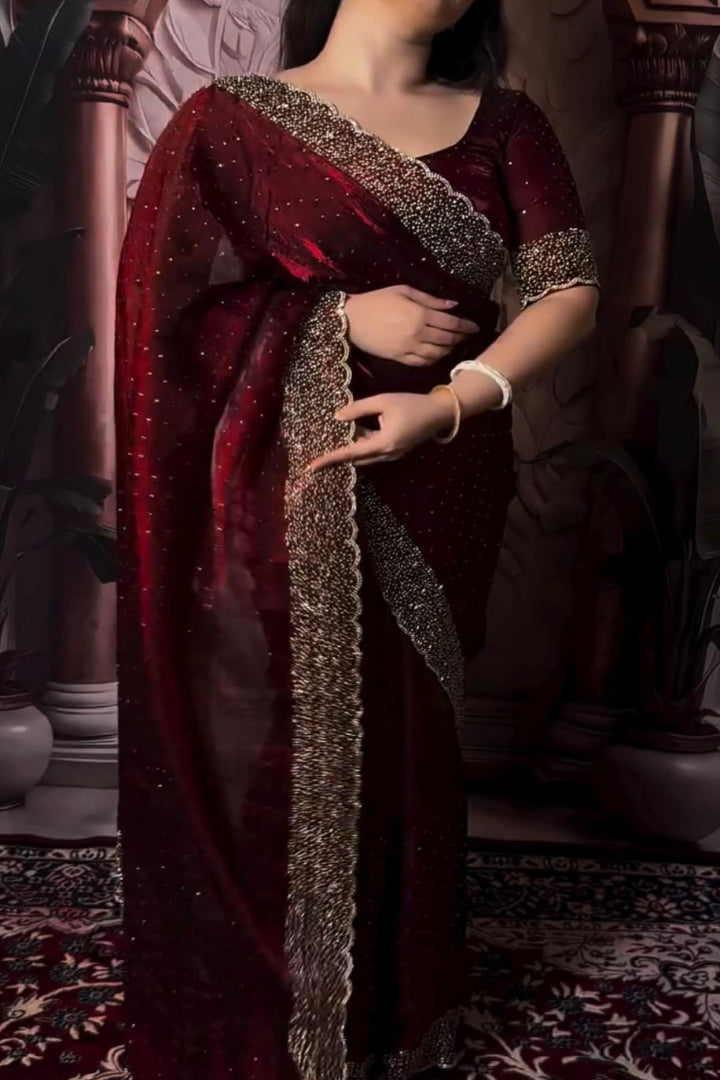 Woman wearing a red saree with intricate patterns, standing indoors.