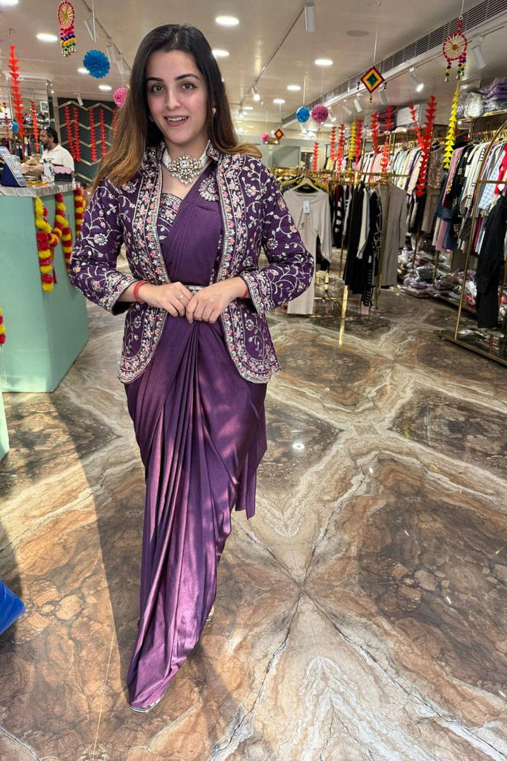 Woman in a purple saree standing in a store with clothing racks in the background
