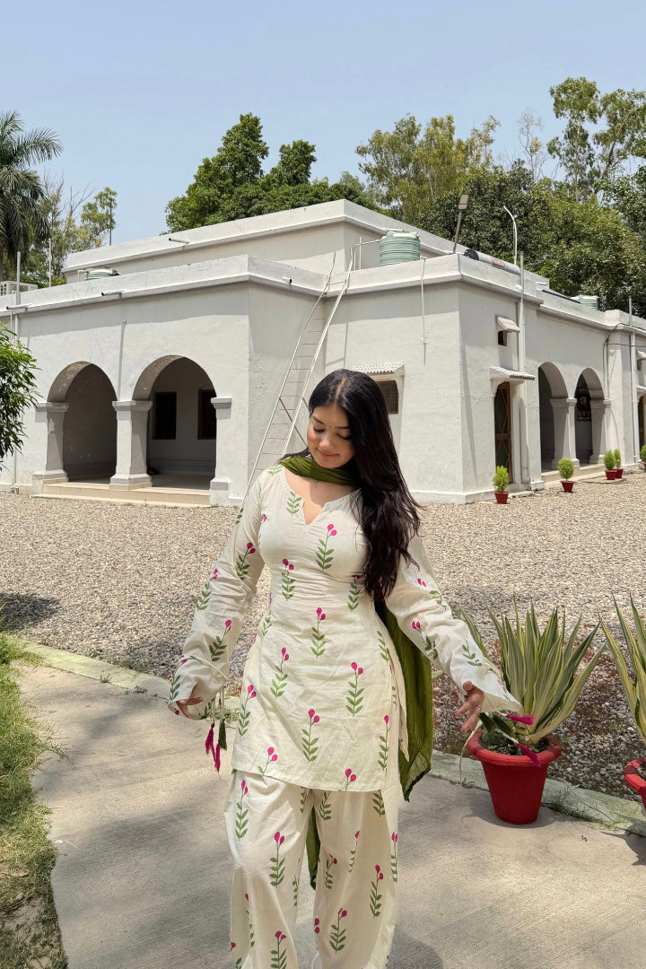 Woman in a floral outfit walking outdoors with a building and trees in the background