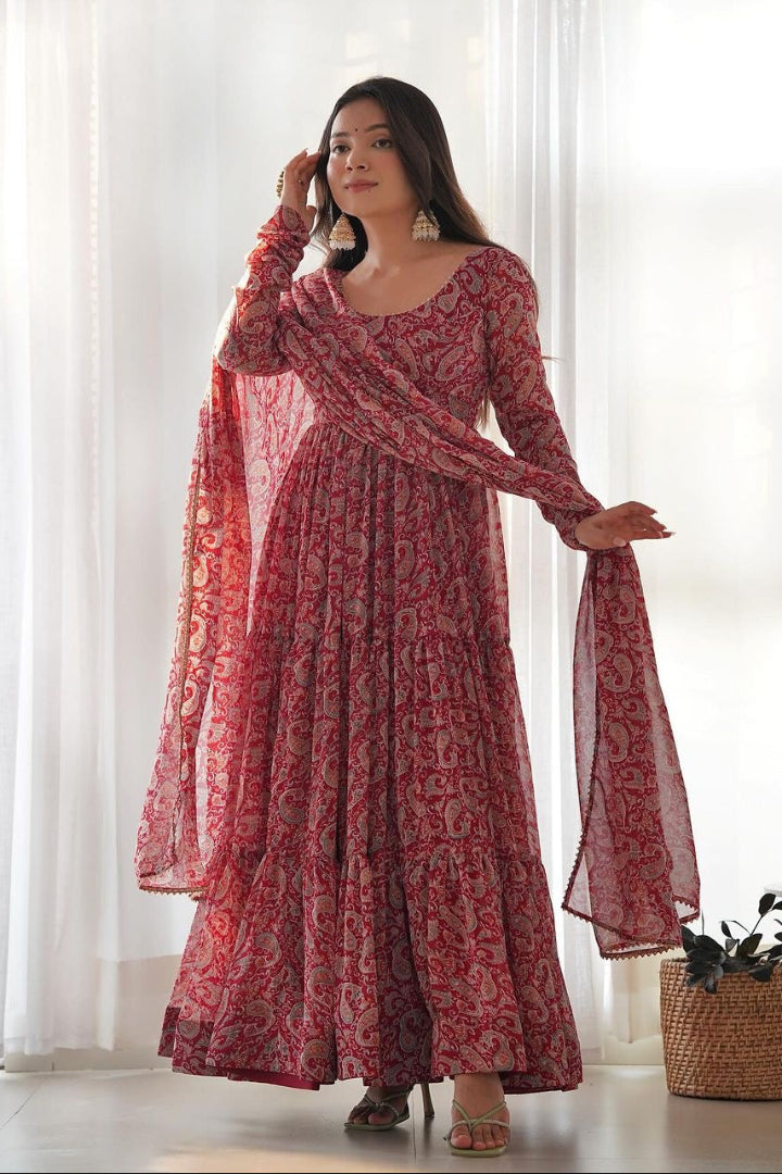 Woman wearing a red patterned dress with a matching dupatta in a bright room.