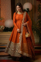 Woman in an orange traditional outfit with gold details at a decorated event.