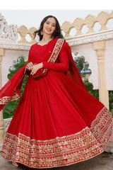 Woman in a red traditional outfit with gold embroidery standing in front of decorative architecture.