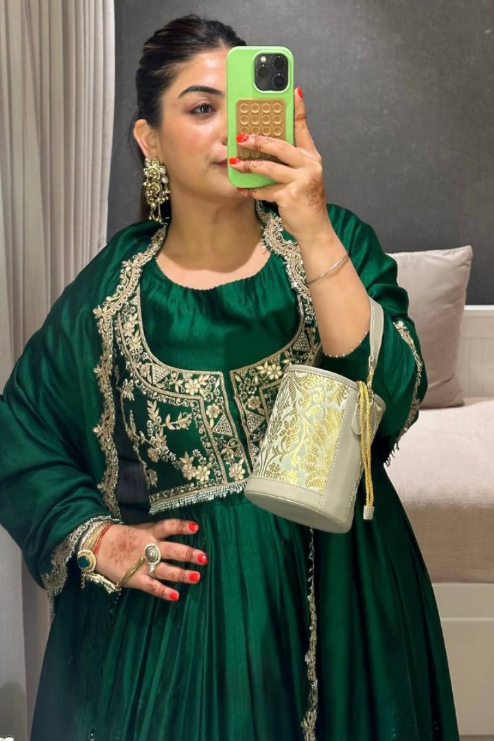 Woman in a green traditional outfit holding a phone and a light-colored bag.