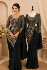 A woman and a mannequin display matching black and beige embroidered traditional sari gowns in an elegant indoor studio setting with neutral beige walls, draped fabric, and decorative floral arrangements.