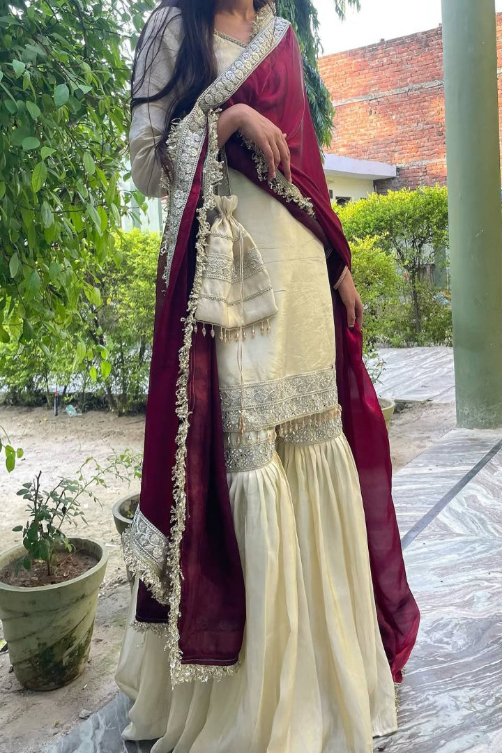 Woman in traditional outfit with maroon dupatta and white saree standing outdoors.