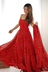 Woman wearing a red patterned dress holding a matching scarf against a white background