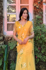Woman in a yellow saree standing outdoors with greenery and a window in the background