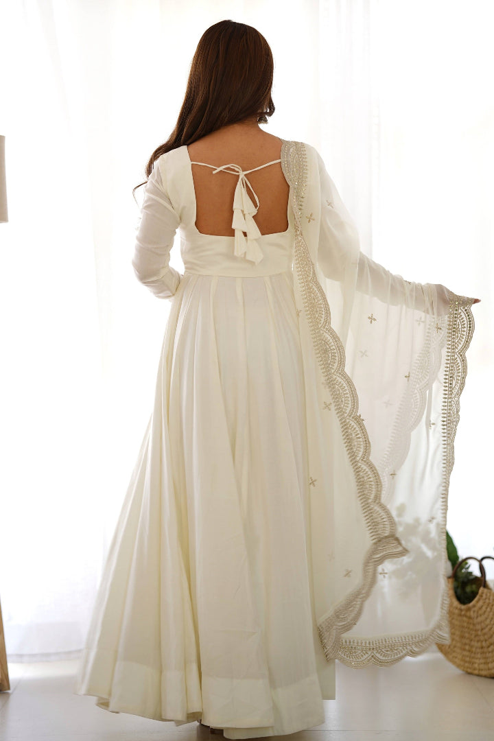 Woman wearing a white dress with a sheer overlay in a bright room.