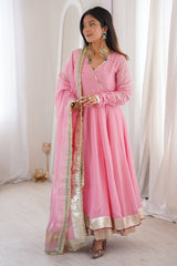 Woman in a pink traditional outfit with gold details in a bright room.
