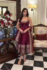 Woman in a maroon traditional outfit standing in a decorated room with floral arrangements and furniture.