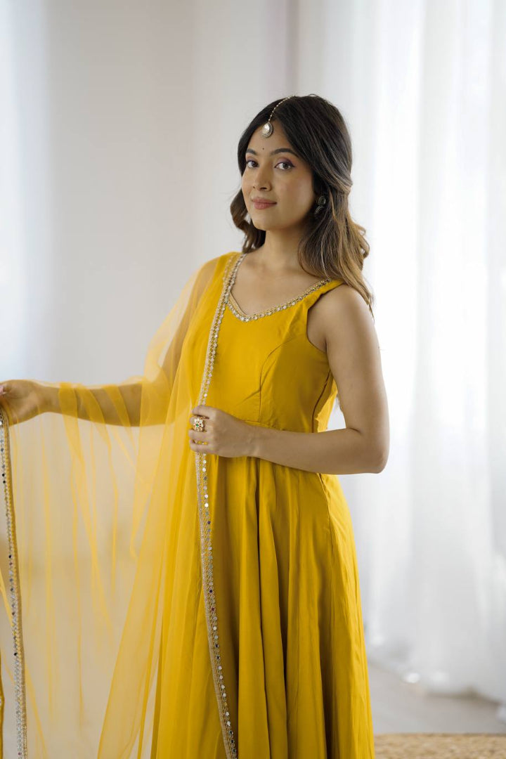 Woman wearing a yellow dress with a matching dupatta, standing against a white curtain.