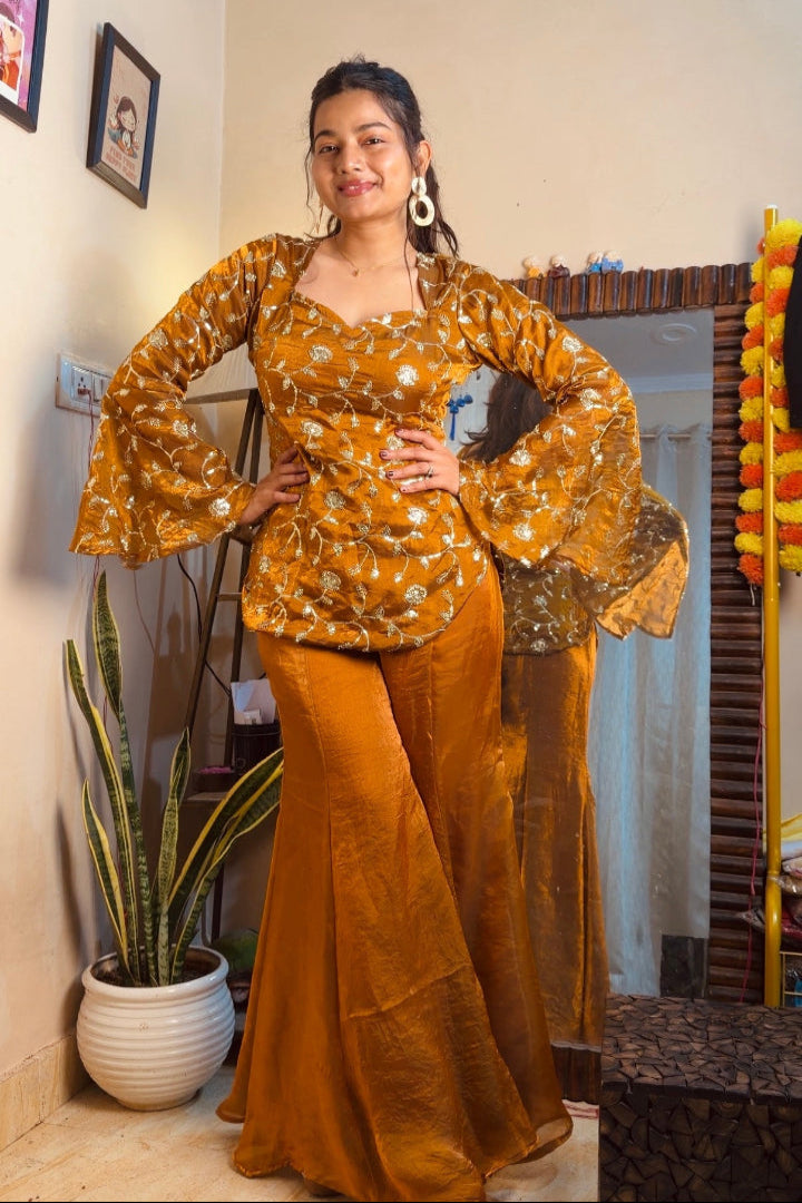 Woman in a mustard yellow traditional outfit standing indoors with decor elements.