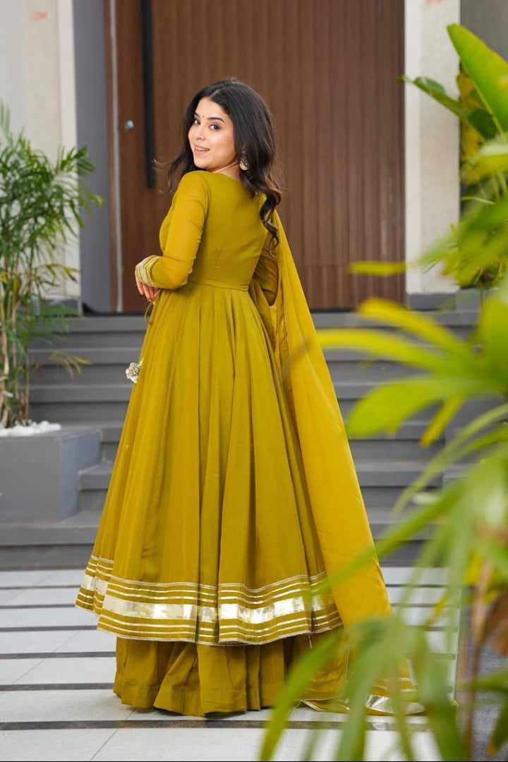 Woman in a yellow traditional outfit standing outdoors with plants and a door in the background