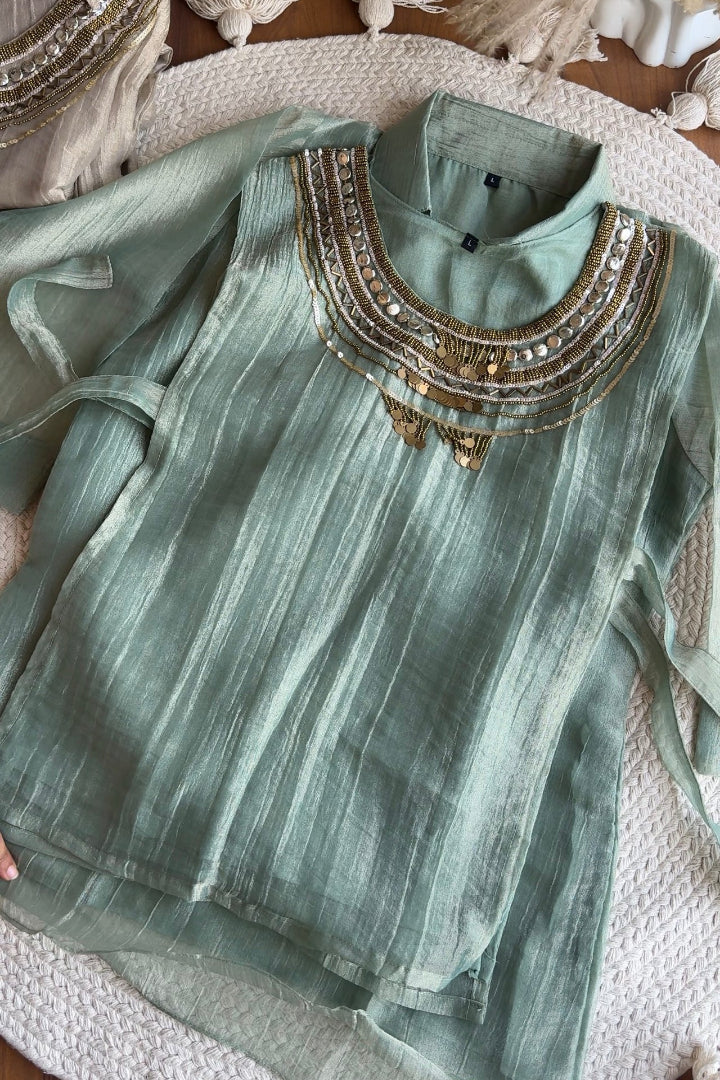 A sage green long-sleeve kurta with vertical stripes and gold metallic embroidery around the high neckline, laid flat on a textured white woven rug.