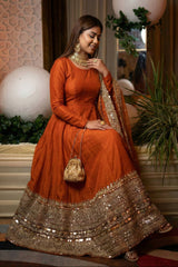 Woman in an orange traditional outfit with gold details indoors.