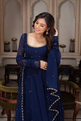 Woman in a blue traditional outfit with intricate designs in an ornate room.