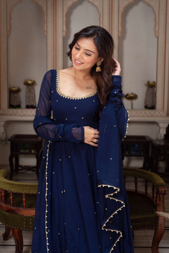 Woman in a blue traditional outfit with intricate designs in an ornate room.