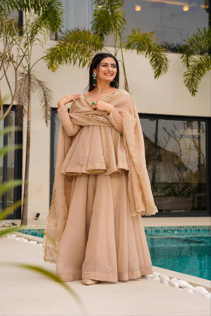 Woman in a beige traditional outfit standing by a pool with greenery around.