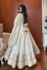 Woman in a white and gold traditional outfit standing in a room with wooden walls.