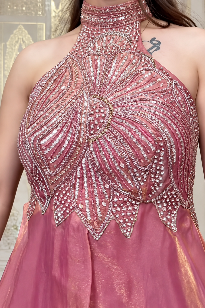 A close-up of a pink halter-neck gown with intricate silver and gold beaded embellishments on the bodice, worn by a model.