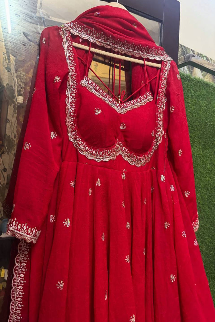 Red embroidered traditional outfit on a hanger against a green and brown background