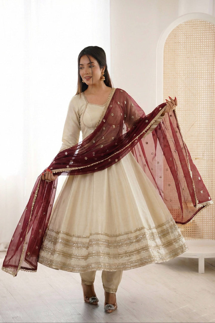 Woman wearing a traditional outfit with a maroon dupatta in a bright room.