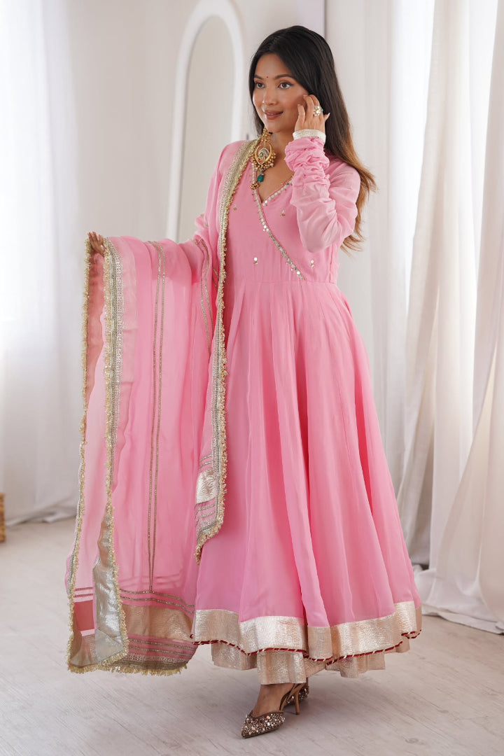 Woman wearing a pink traditional outfit with gold details in a bright room.