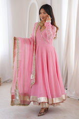 Woman wearing a pink traditional outfit with gold details in a bright room.