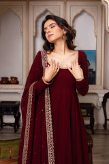 Woman in a maroon traditional outfit with gold embroidery in an ornate room.