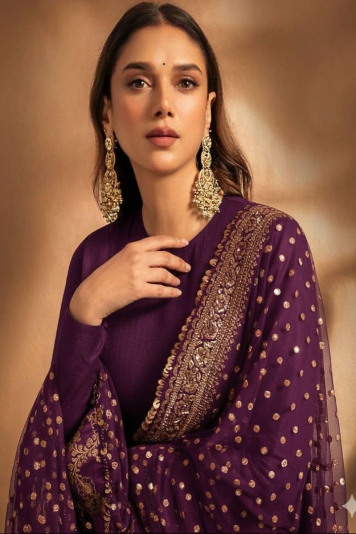 Woman wearing a purple saree with gold embroidery against a warm brown background