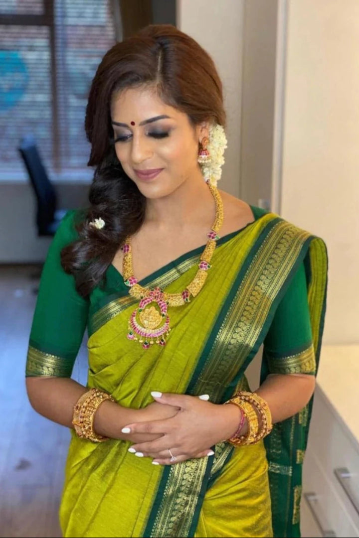 Woman in a green and yellow saree with jewelry indoors