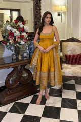 Woman in a yellow traditional outfit standing in an elegant room with floral arrangements and decorative furniture.
